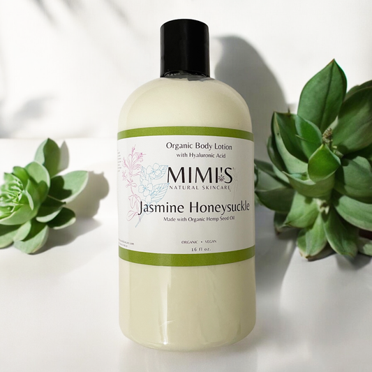 A bottle of organic body lotion with hyaluronic acid and wild rose, branded as MIMIS Natural Skincare, with a pump dispenser, placed next to green foliage.
