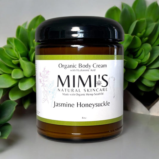 Jar of Mimi's Natural Skincare Organic Body Cream with Jasmine Honeysuckle scent, surrounded by green plants.