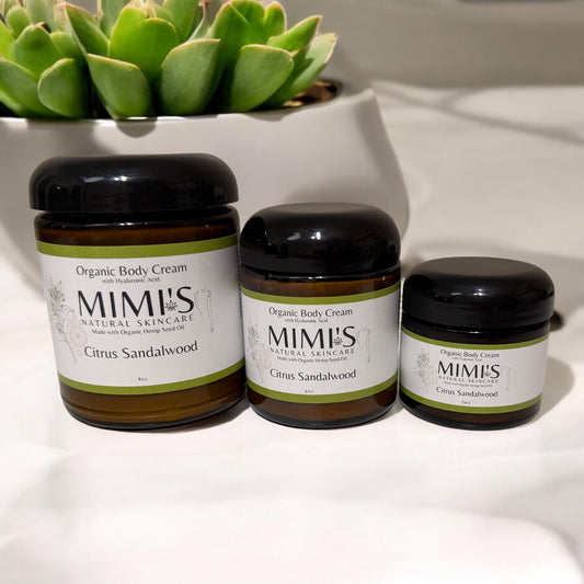 Three jars of MIMI's Citrus Sandalwood Organic Body Cream on a white surface with a succulent plant in the background.