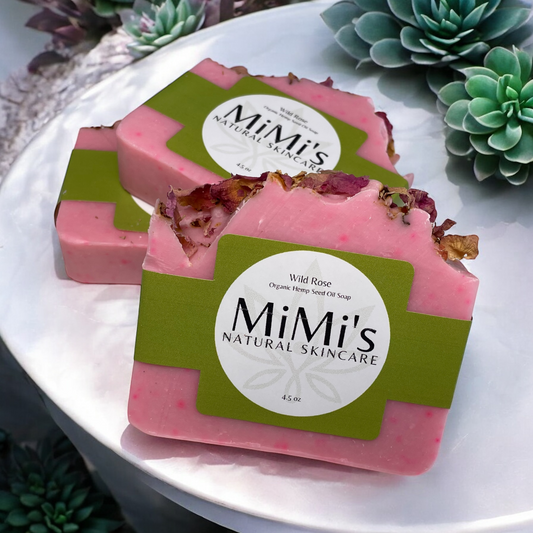 Bars of handmade soap with a pink hue and floral inclusions, wrapped with a green label that reads 'MiMi's Natural Skincare'.